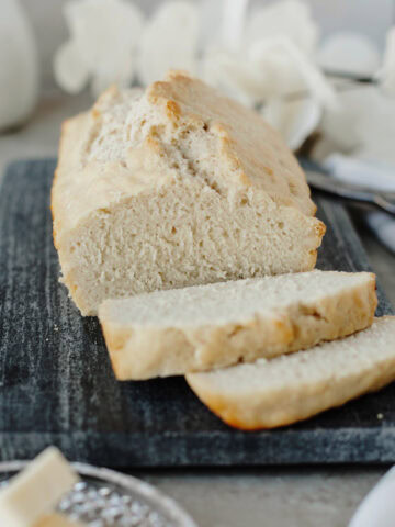 A sliced loaf of beer bread ready to serve from a wood cutting board.