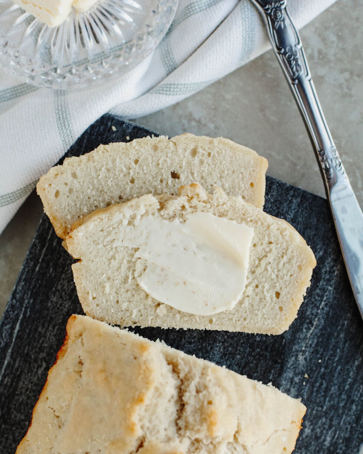 Sliced beer bread with butter on a black cutting board.