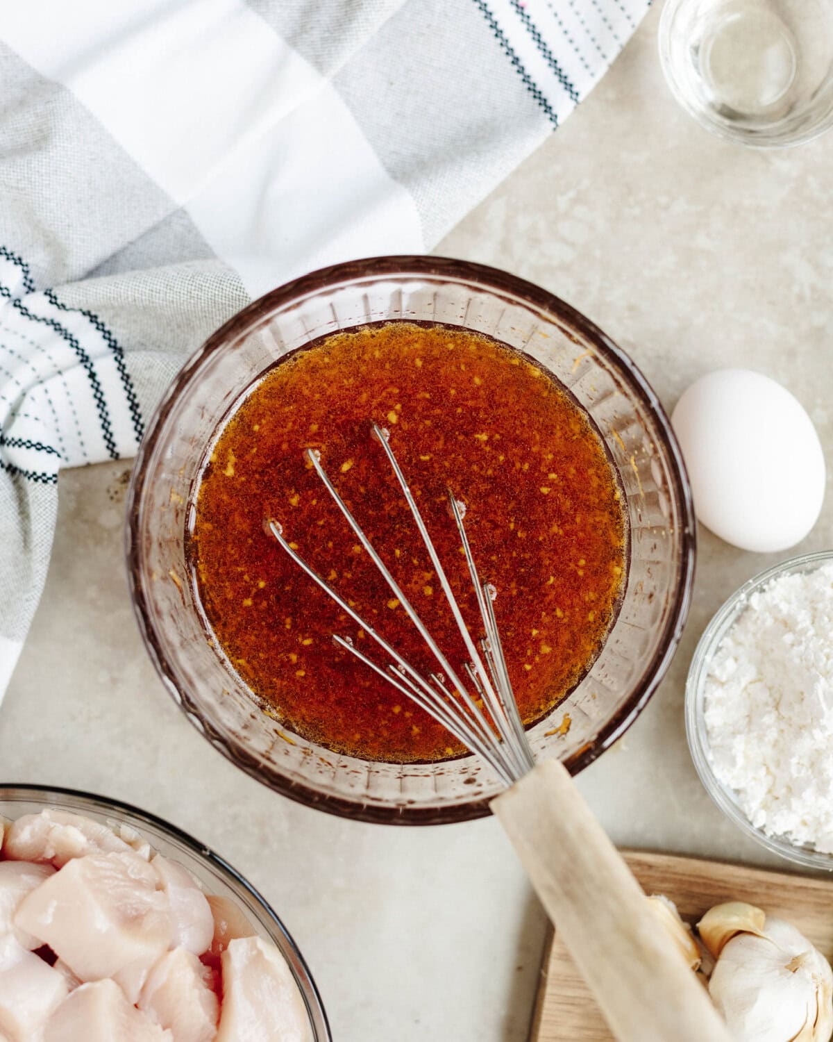 Water, sesame oil, sugar, vinegar, and orange zest combined in a glass bowl using a whisk.