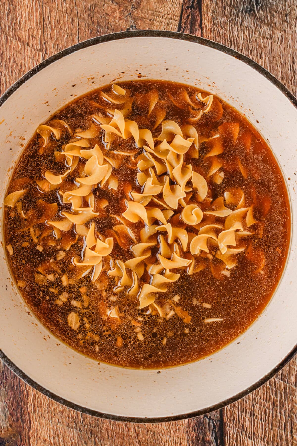 Beef broth added to egg noodles, beef stew meat, and seasonings in a Dutch oven.