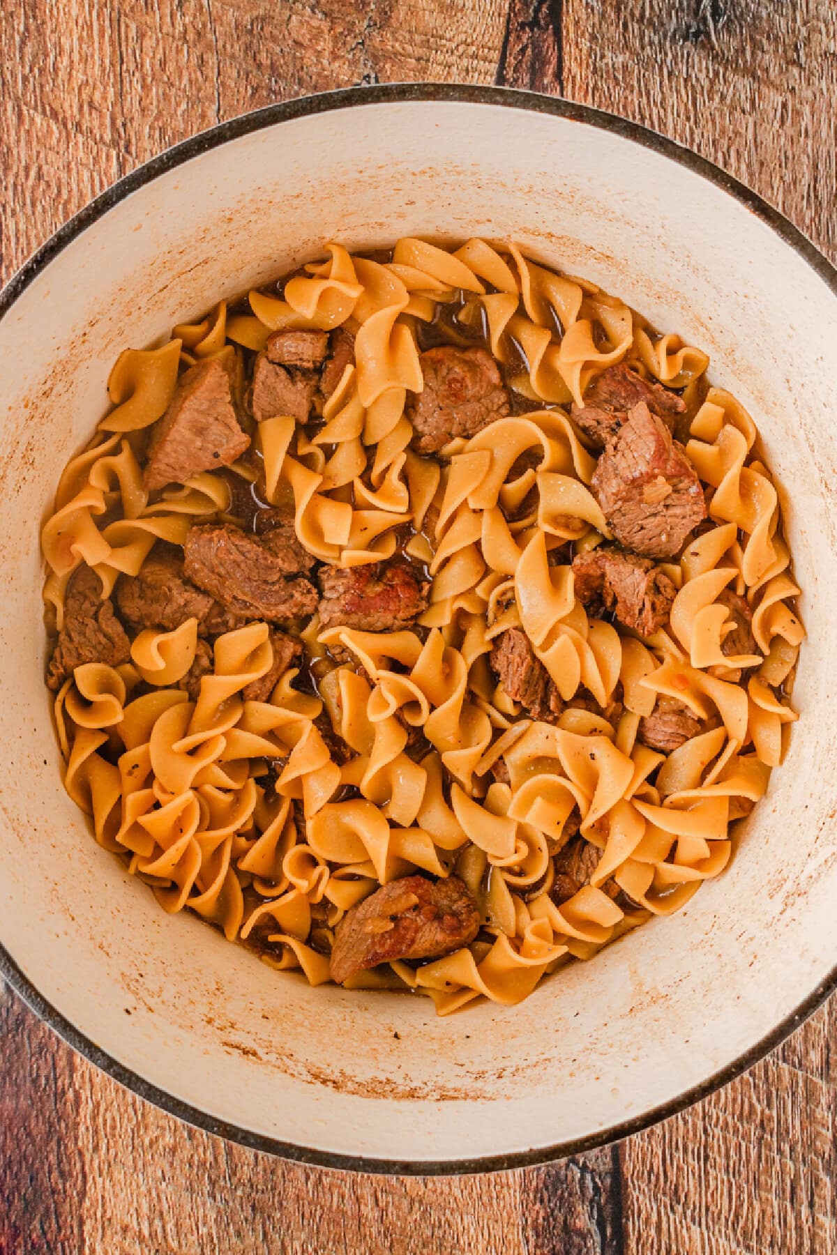 Tender pasta combined with cooked stew meat in a Dutch oven.