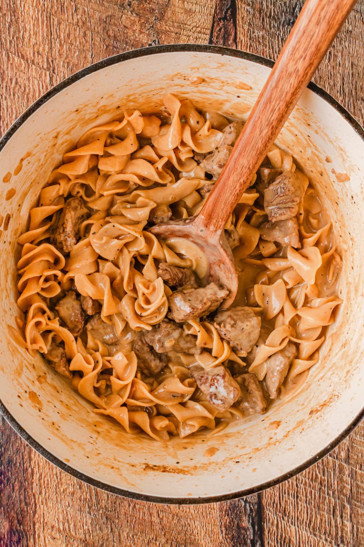 A Dutch oven with pasta, stew meat, and a creamy sauce combined.