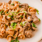 French onion beef and noodles served on a white dinner plate.