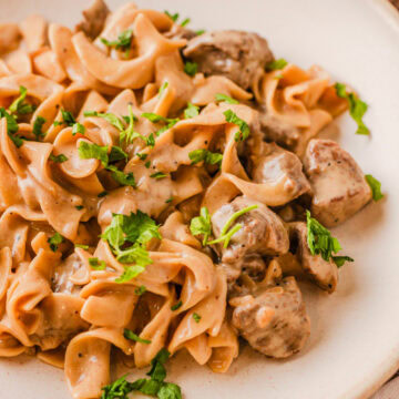 French onion beef and noodles served on a white dinner plate.