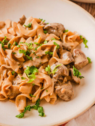 French onion beef and noodles served on a white dinner plate.