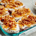 Onion dip, cheddar cheese, and fried onions sprinkled on top of boneless pork chops in a 9x13 baking pan.