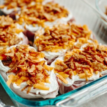 Onion dip, cheddar cheese, and fried onions sprinkled on top of boneless pork chops in a 9x13 baking pan.