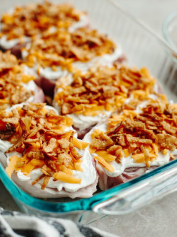 Onion dip, cheddar cheese, and fried onions sprinkled on top of boneless pork chops in a 9x13 baking pan.