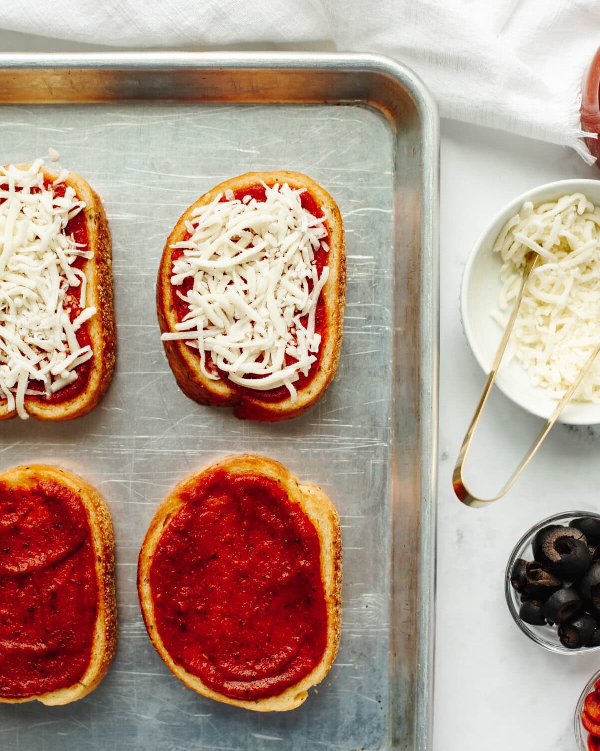Pizza sauce and shredded Mozzarella sprinkled on top of garlic bread.