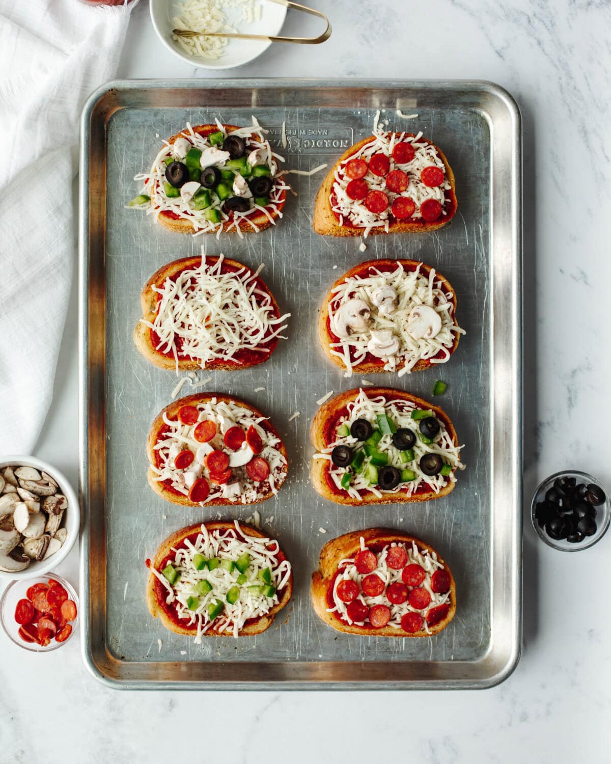 Pepperoni, cheese, bell peppers, and olives sprinkled on top of slices of garlic toast.