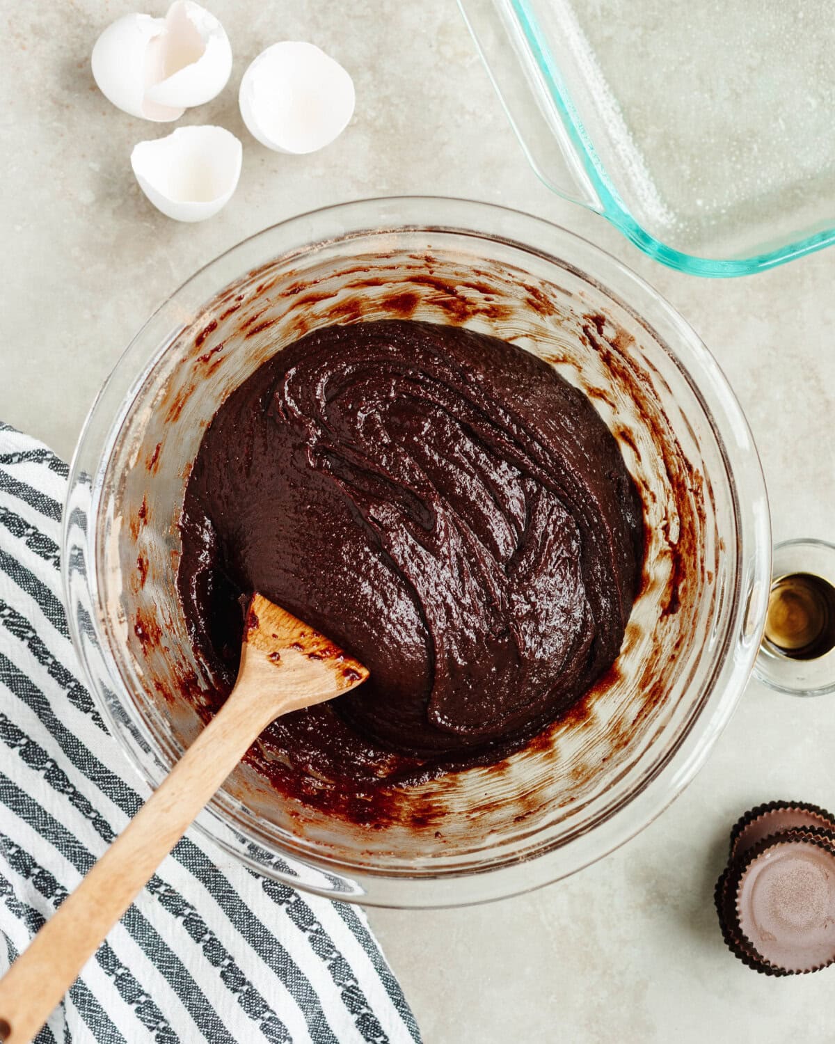 Brownie batter combined in a glass mixing bowl using a wooden spoon.