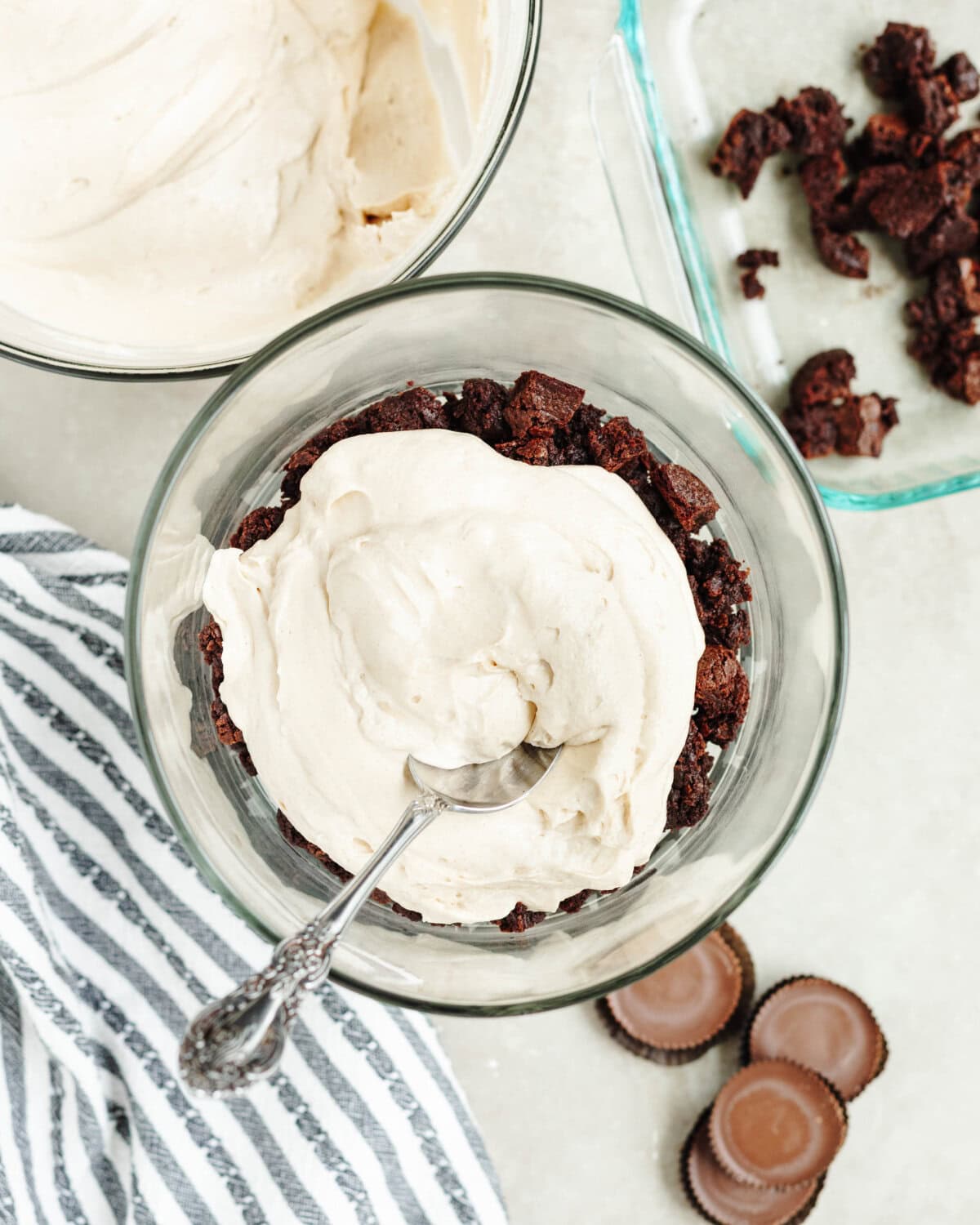 A peanut butter mixture spread evenly on top of chopped brownies in a glass bowl.
