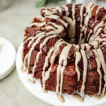 Icing drizzled on top of pumpkin spice monkey bread served on a cake stand.