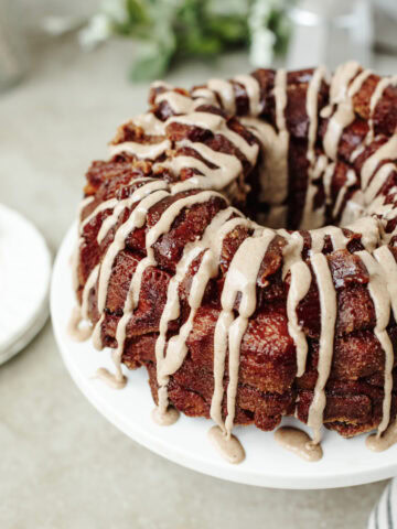 Icing drizzled on top of pumpkin spice monkey bread served on a cake stand.