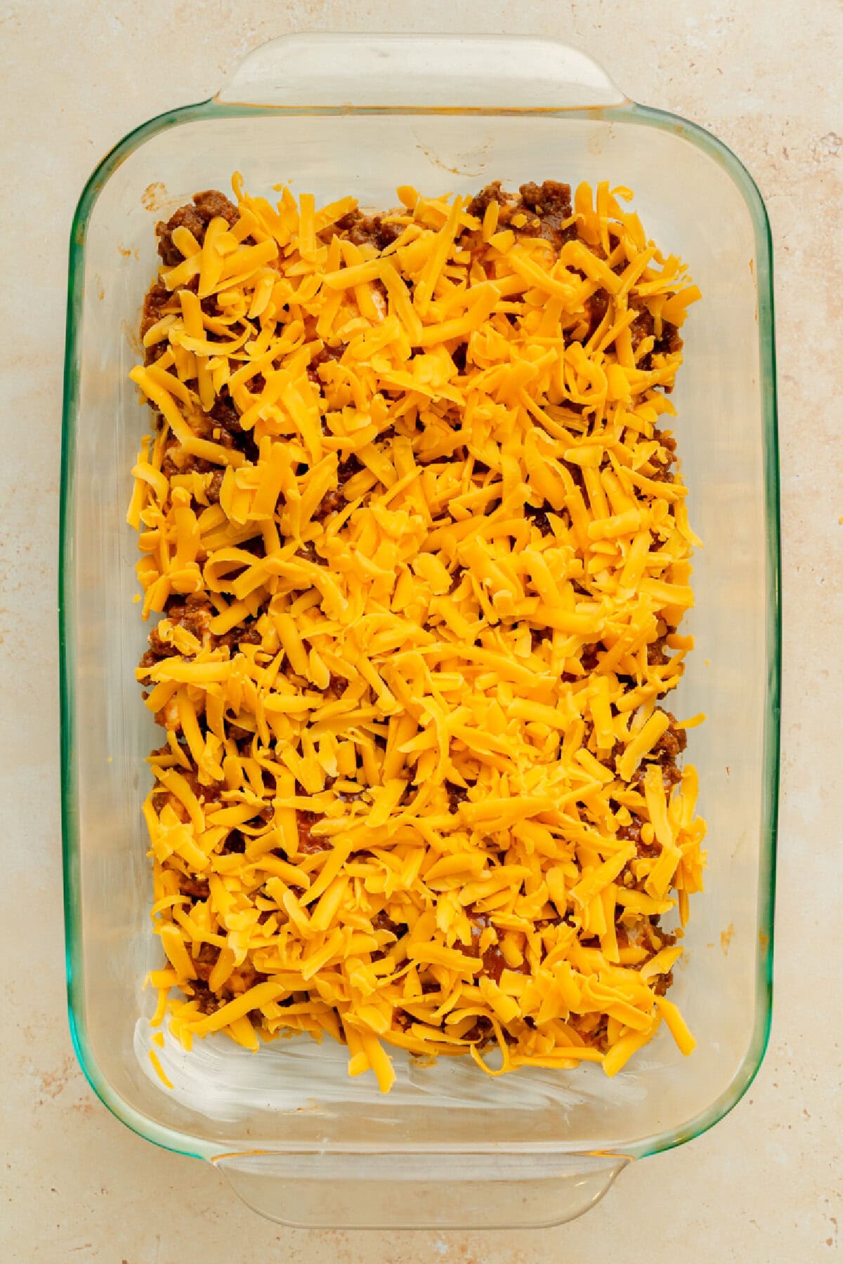 Shredded Cheddar cheese sprinkled on top of a ground beef casserole.