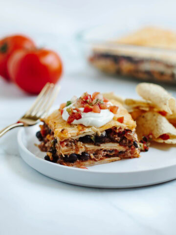 A slice of taco lasagna served on a white plate topped with sour cream and salsa.