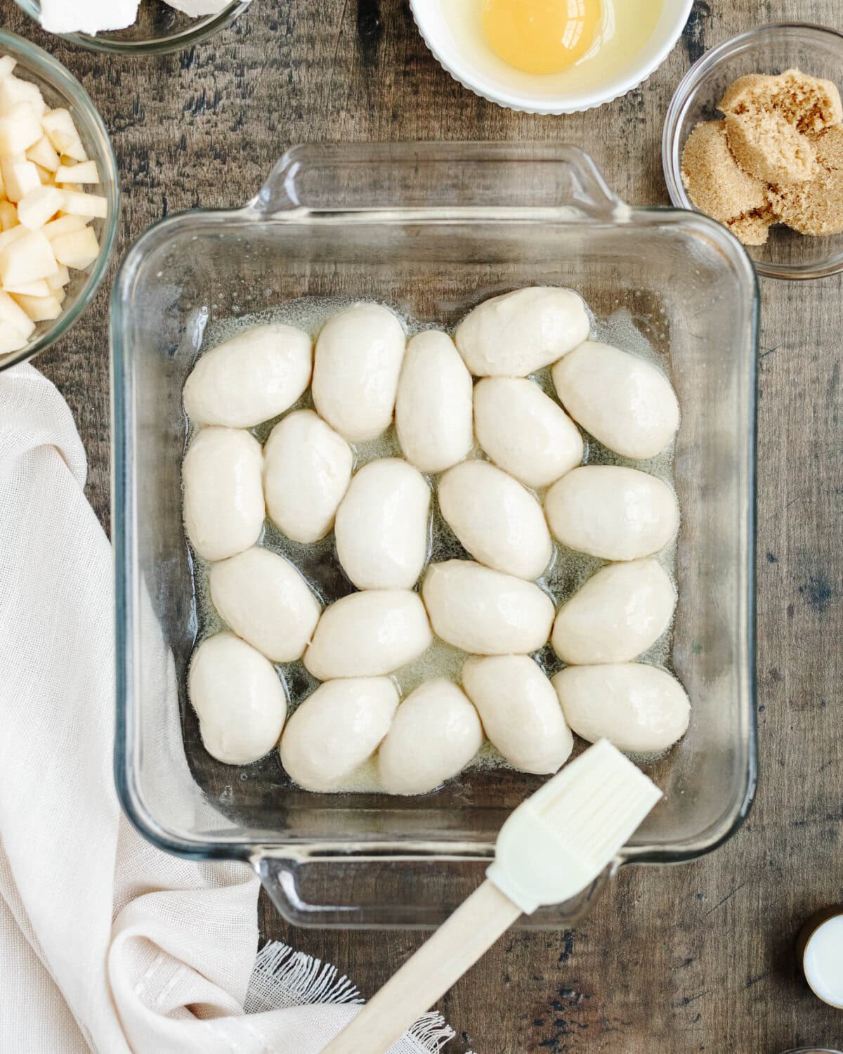 Melted butter brushed on thawed dinner rolls in a glass baking pan.