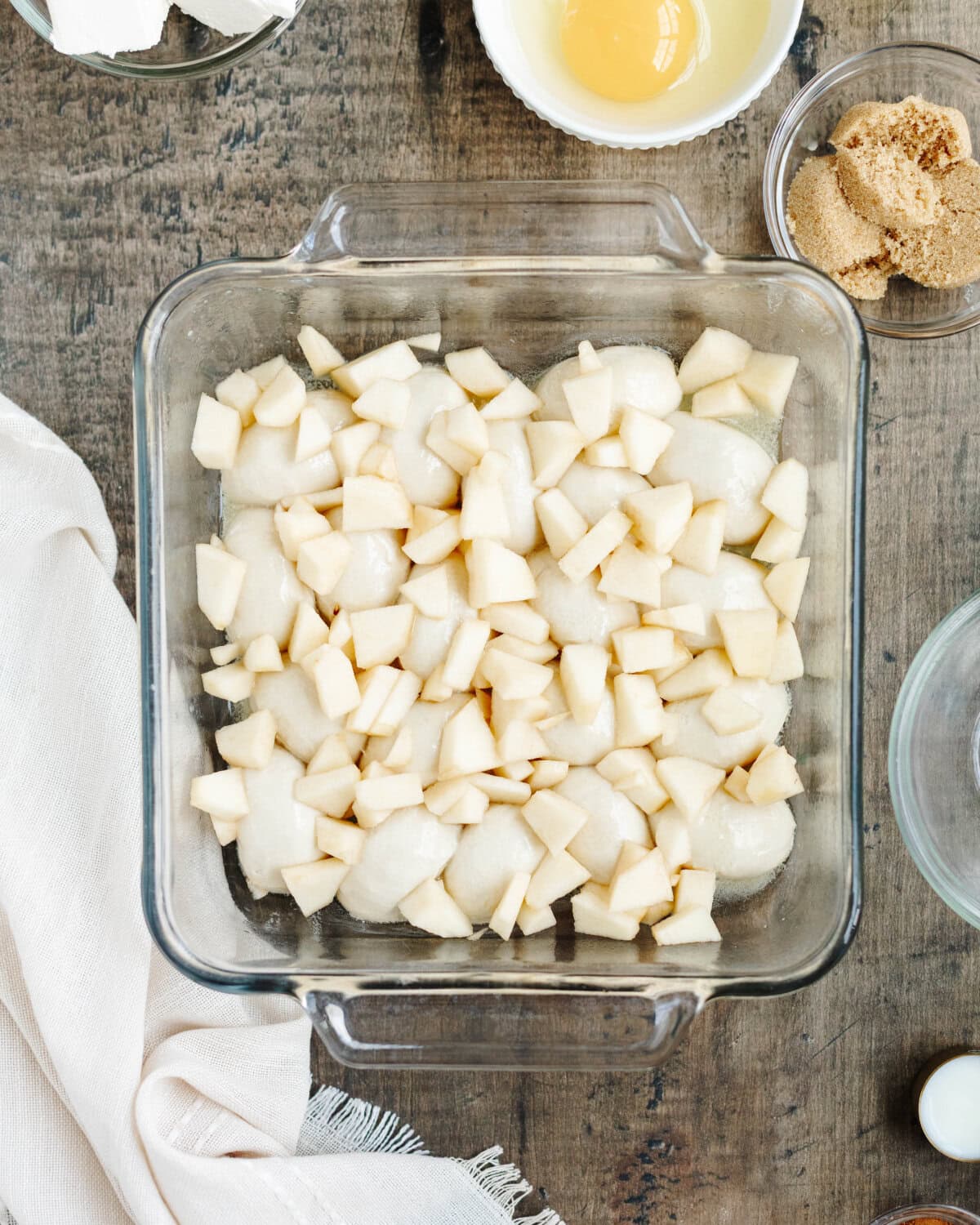 Chopped apples sprinkled on top of thawed dinner rolls in a glass 8x8 baking pan.