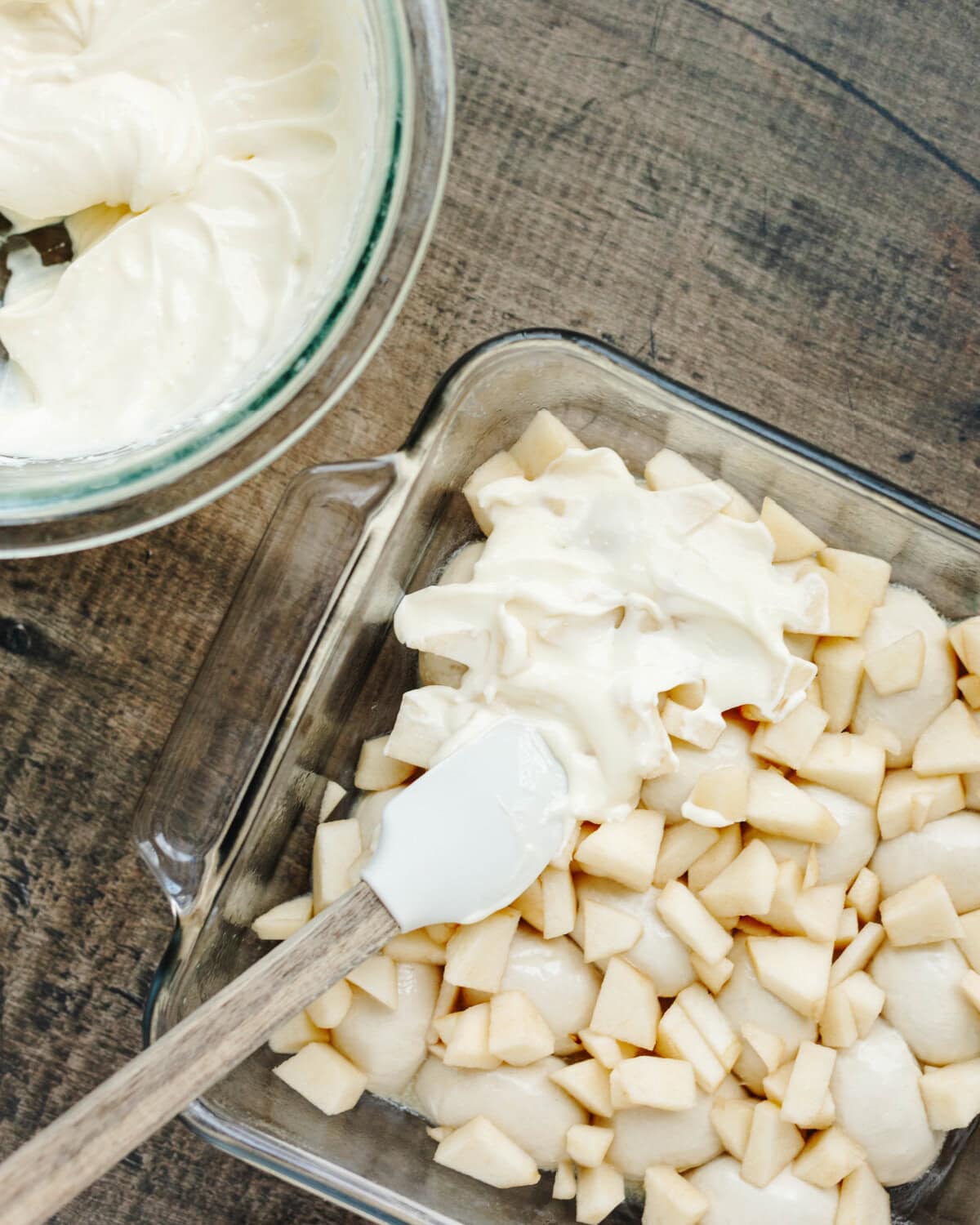 Cream cheese, egg, sugar, and lemon juice mixture spread over chopped apples in a glass baking pan.