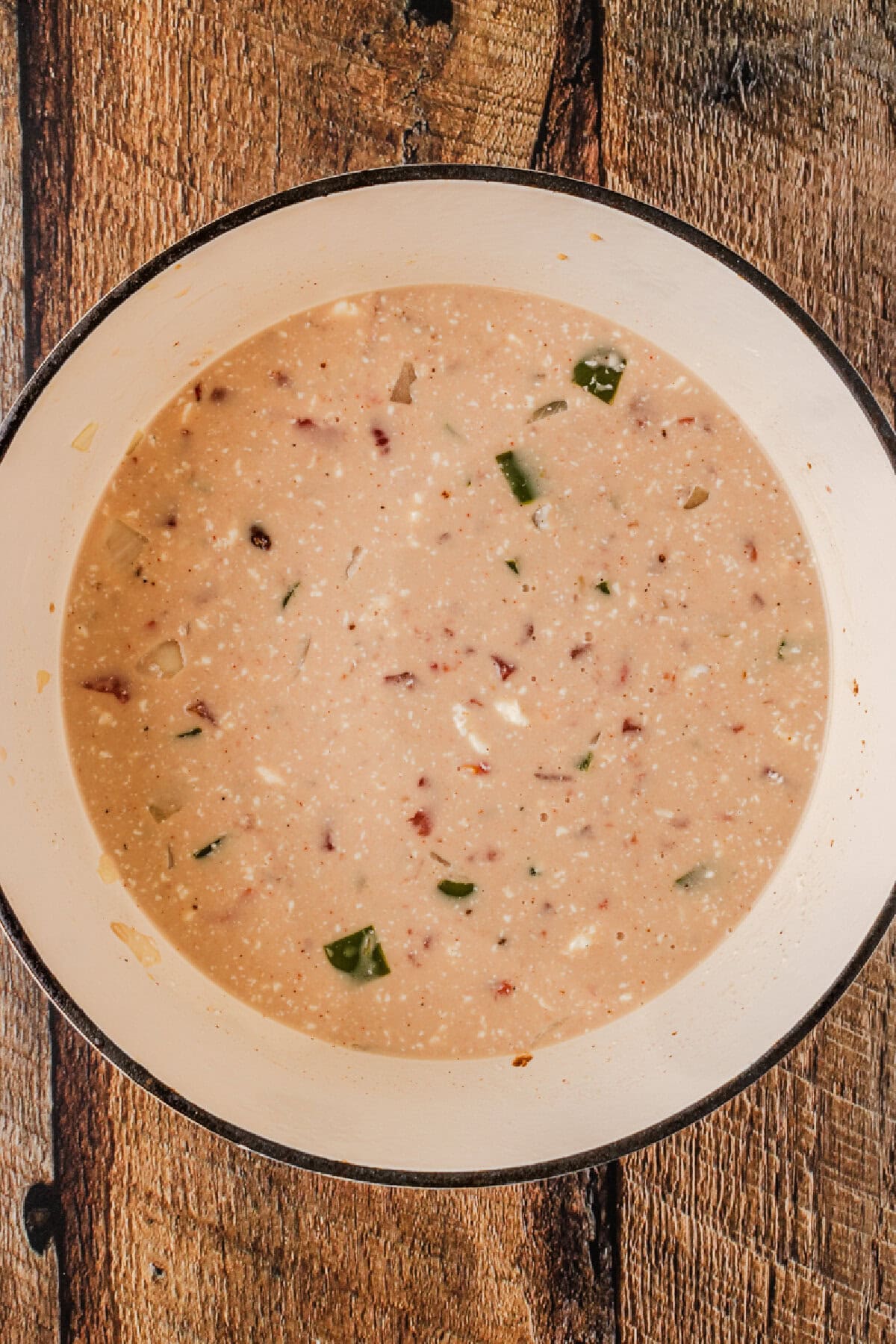 Cream cheese added to a soup mixture in a large pot.
