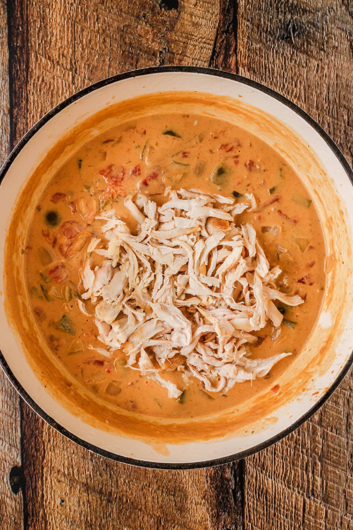 Shredded cooked chicken added to a Dutch oven.