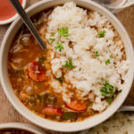 A bowl of chicken and sausage gumbo served over white rice with a spoon.