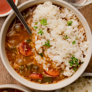A bowl of chicken and sausage gumbo served over white rice with a spoon.