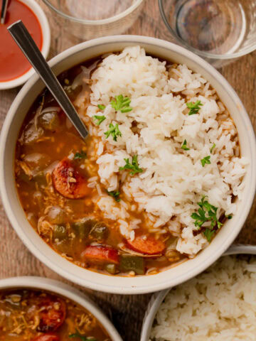 A bowl of chicken and sausage gumbo served over white rice with a spoon.