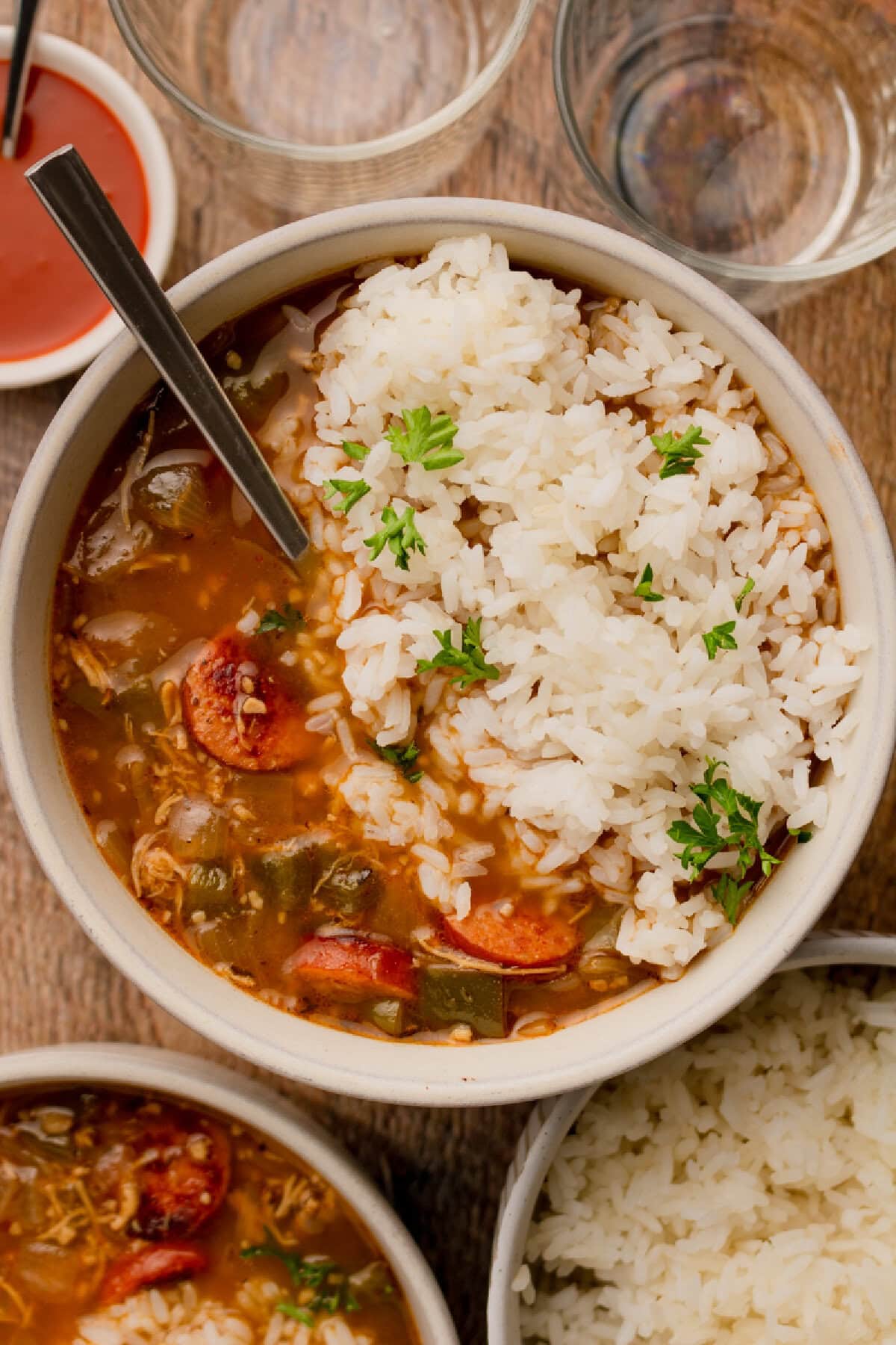 A bowl of chicken and sausage gumbo served over white rice with a spoon.