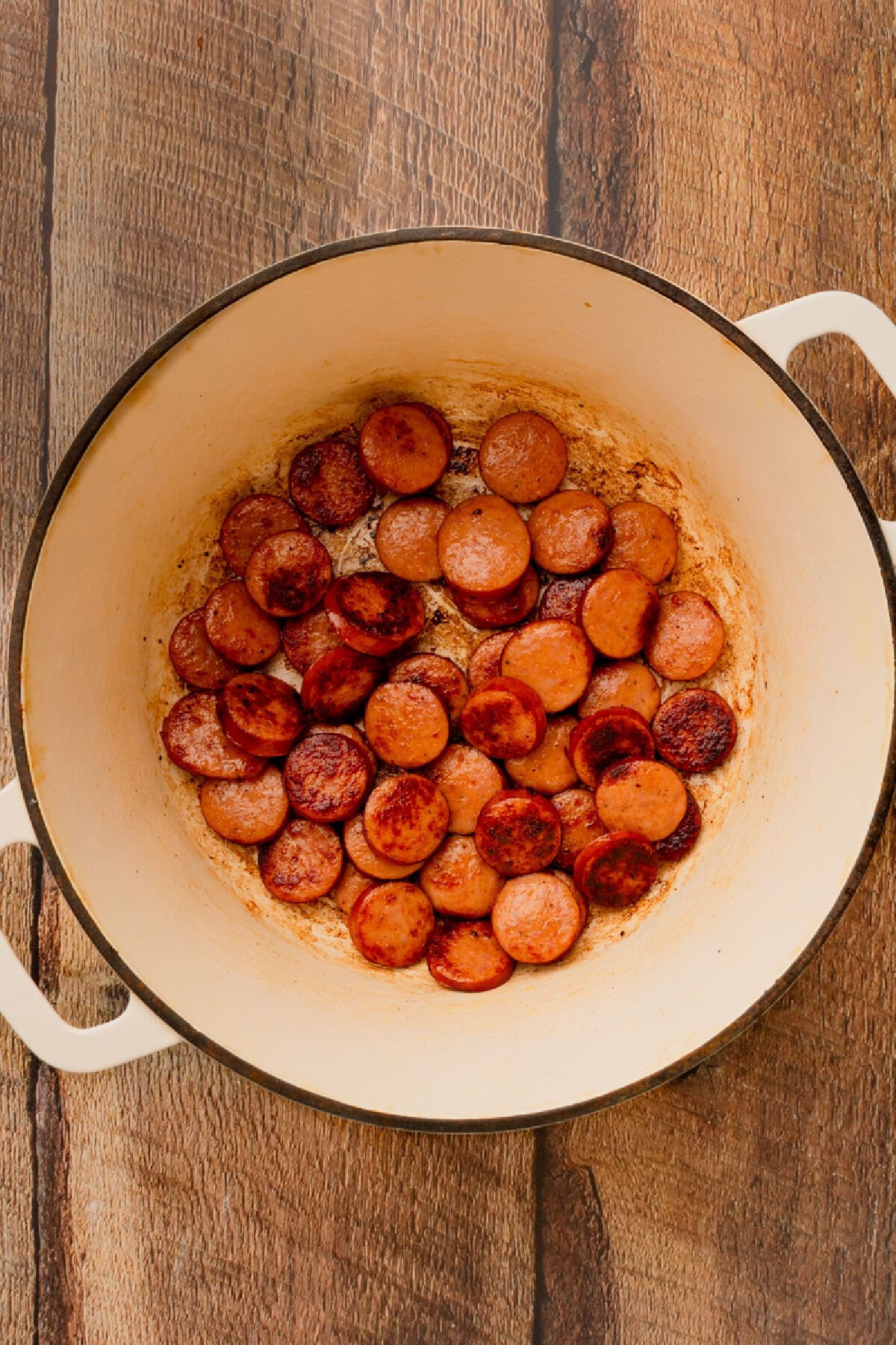 Andouille sausage cooking in a Dutch oven until browned.