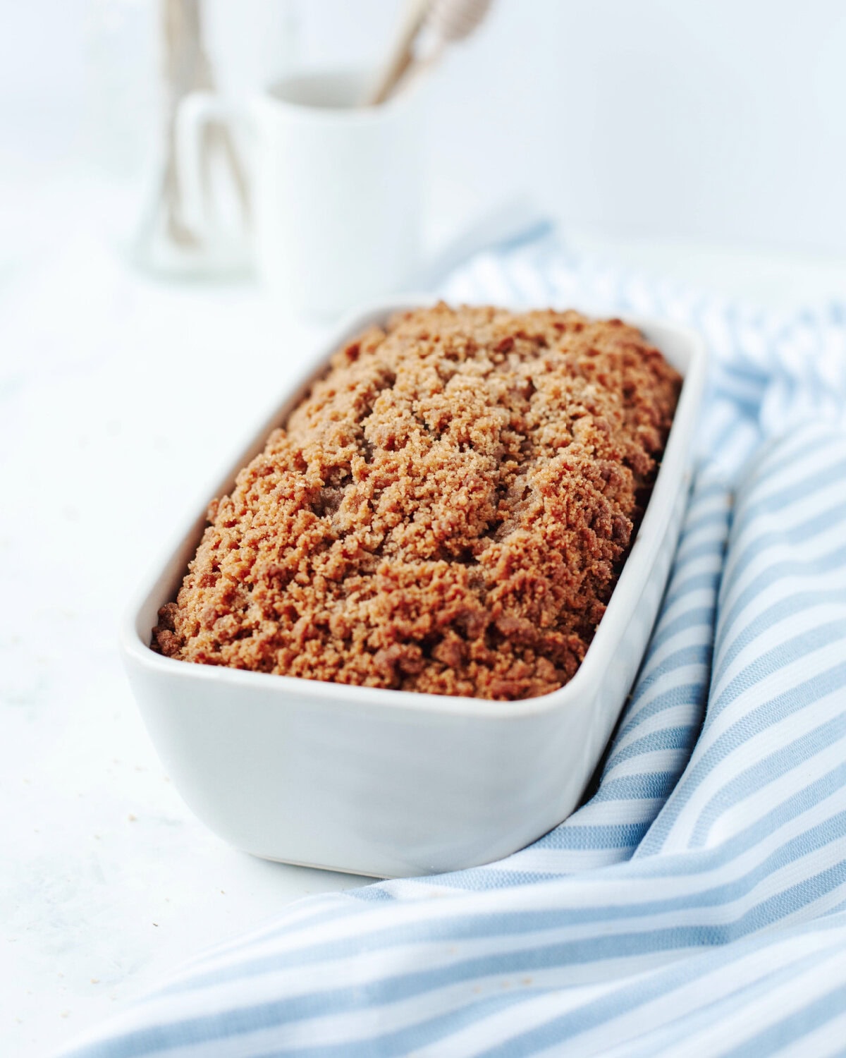 A top view of cinnamon crumble on top of a loaf of moist banana bread in a white loaf pan.