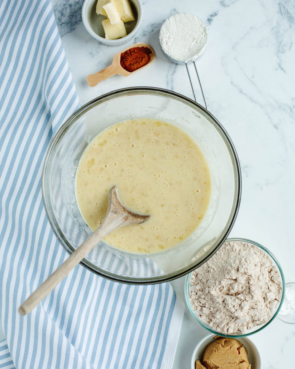 Eggs, banana, sugar, oil, and Greek yogurt combined in a glass bowl.