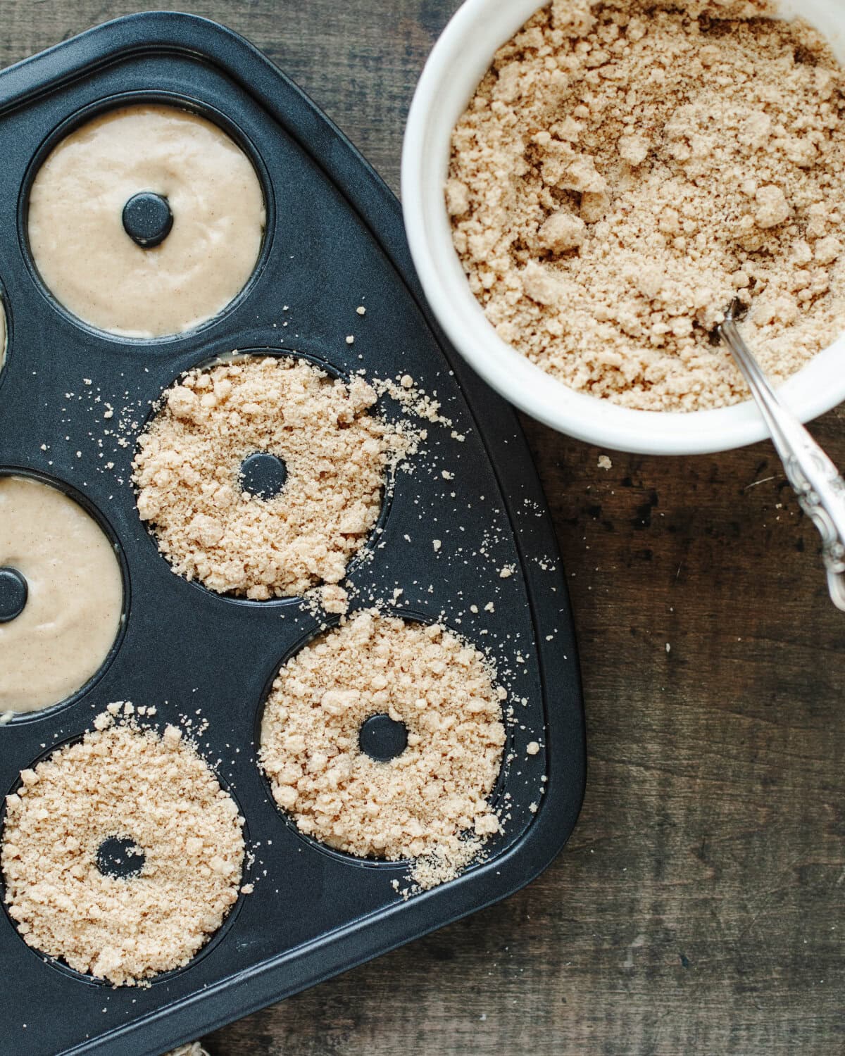 A cinnamon streusel crumb topping sprinkled on top of batter in a doughnut pan.