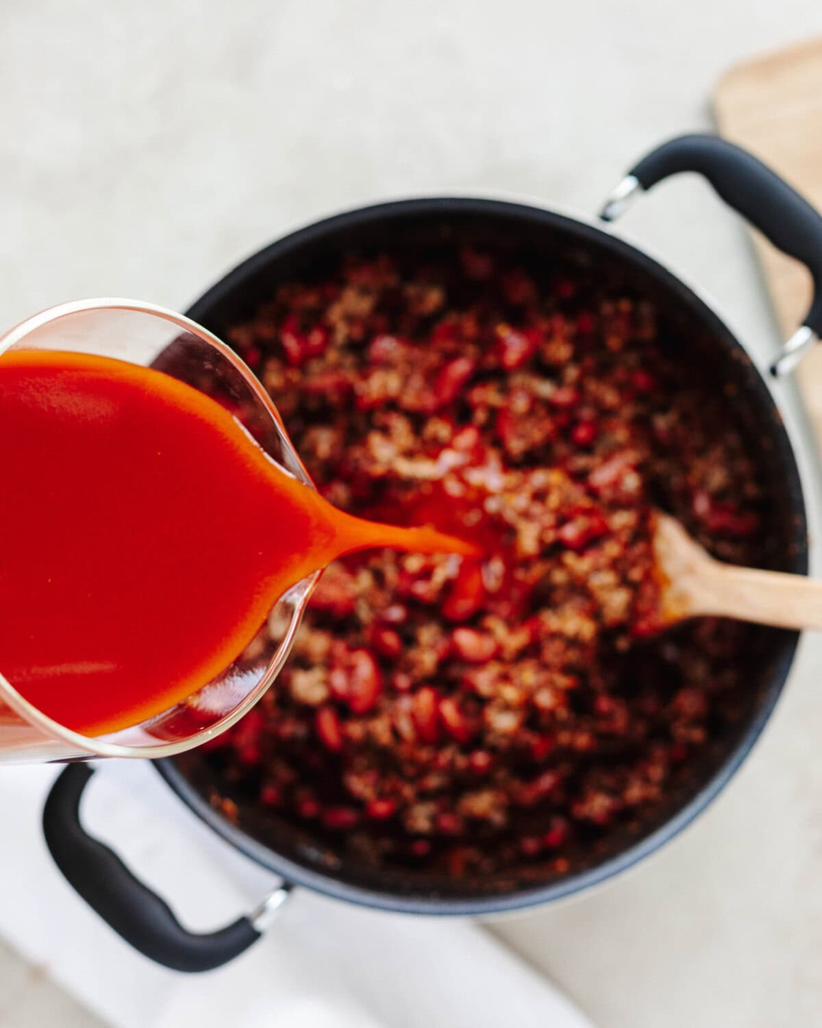 V-8 tomato juice being poured into beef and bean chili.