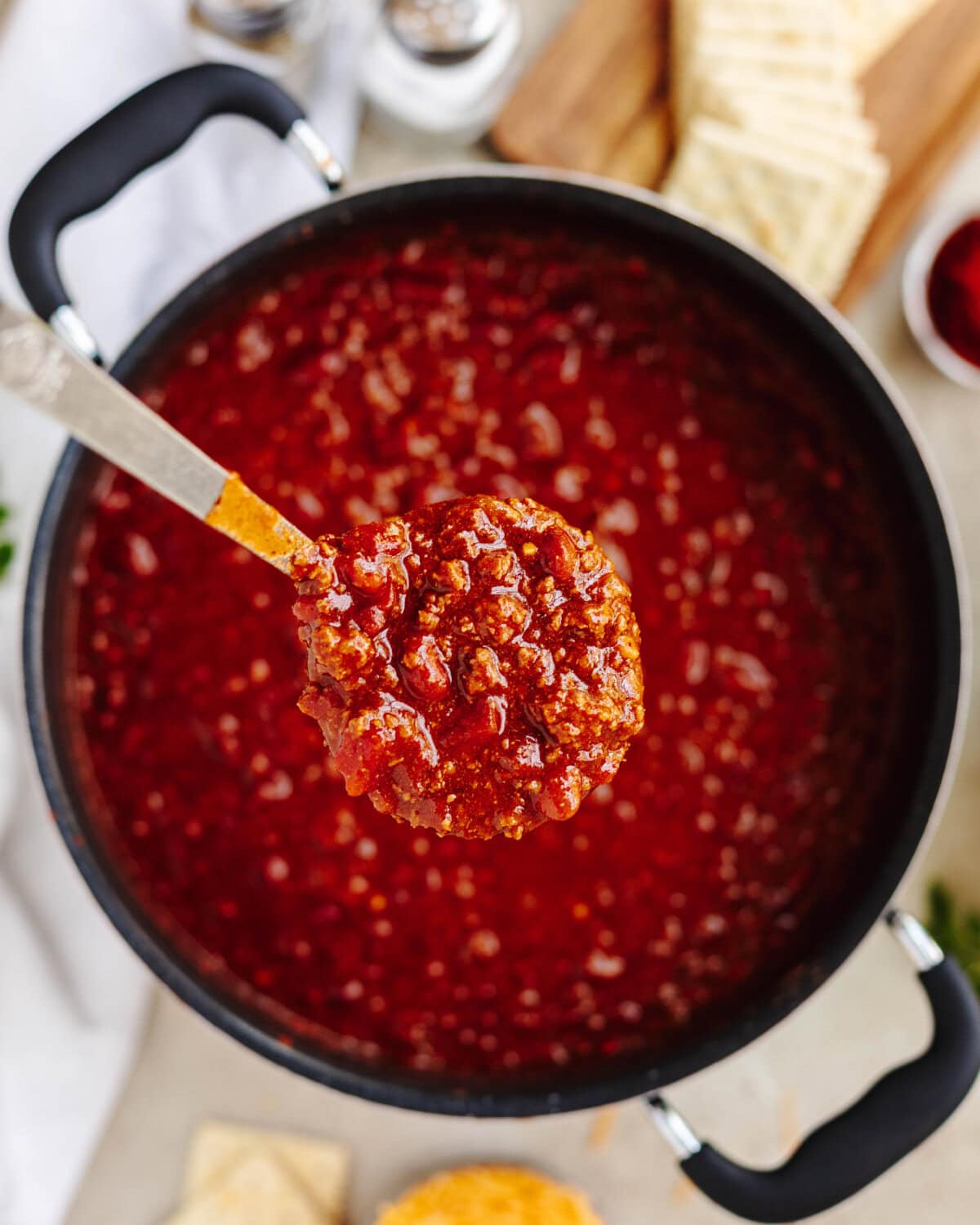 A spoon scooping ground beef chili from a large pot.