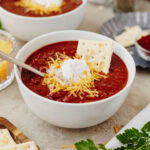 Beef chili topped with shredded cheddar cheese, sour cream, and saltine crackers.