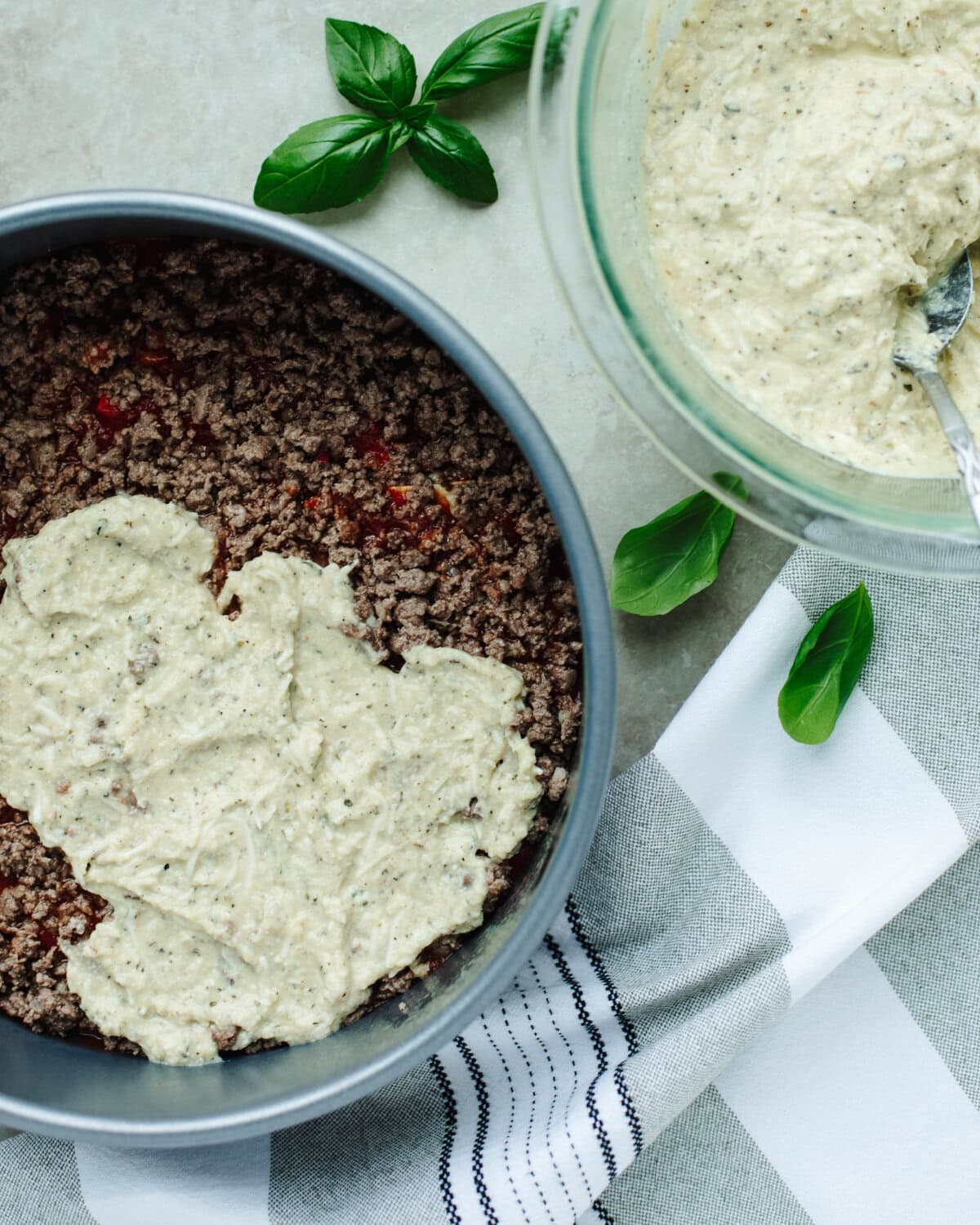 A ricotta cheese mixture spread evenly over cooked ground beef in a springform pan.