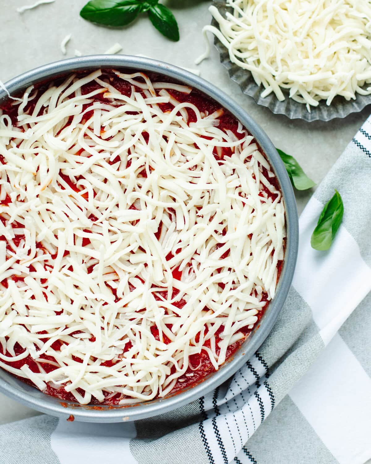 Shredded mozzarella cheese on top of a layer of spaghetti sauce in a springform pan.
