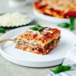 A slice of lasagna on a small white dinner plate ready to enjoy.