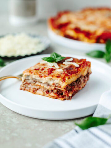 A slice of lasagna on a small white dinner plate ready to enjoy.