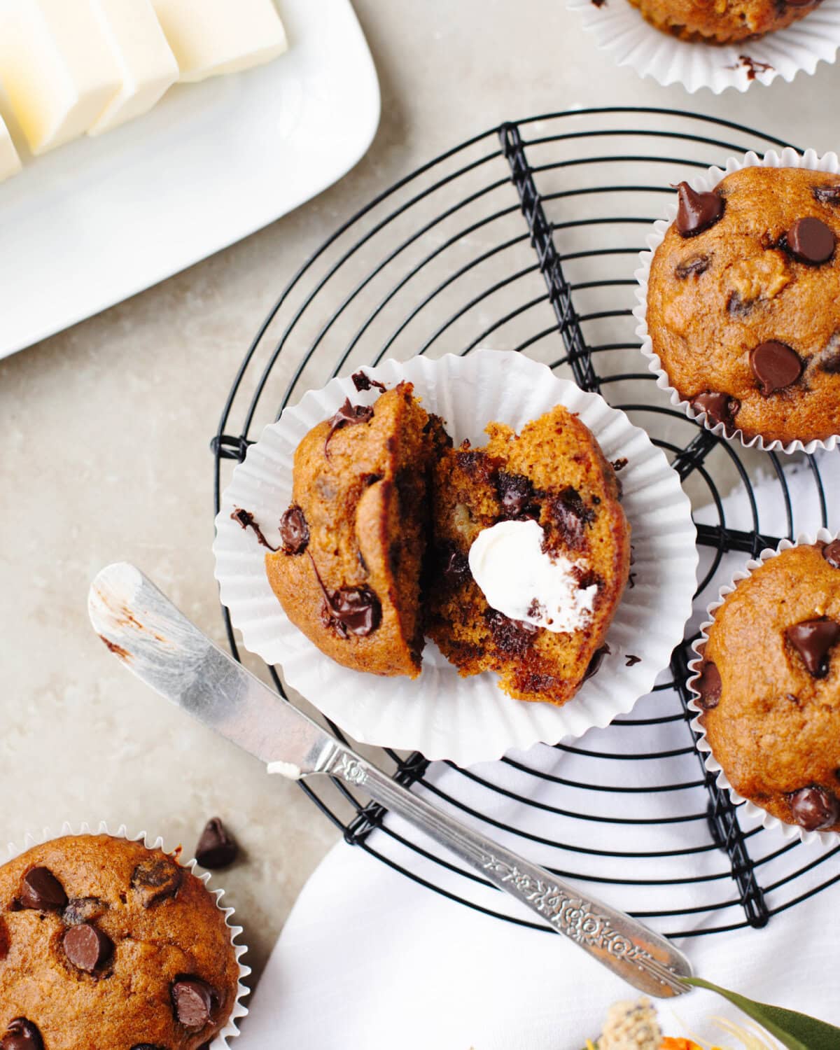 Baked pumpkin banana chocolate chip muffins cooling on a wire rack with one muffin split in half and served with butter.