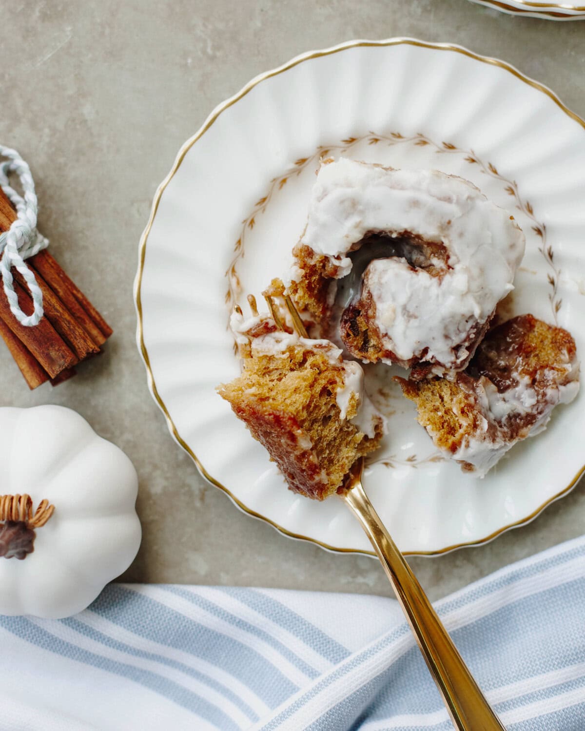 A pumpkin cinnamon roll on a white plate with a fork showing the moist center.