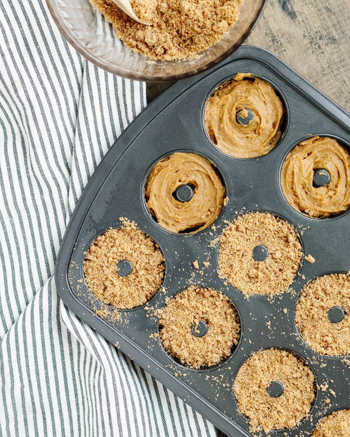 A cinnamon streusel topping sprinkled on top of batter in a prepared doughnut pan.
