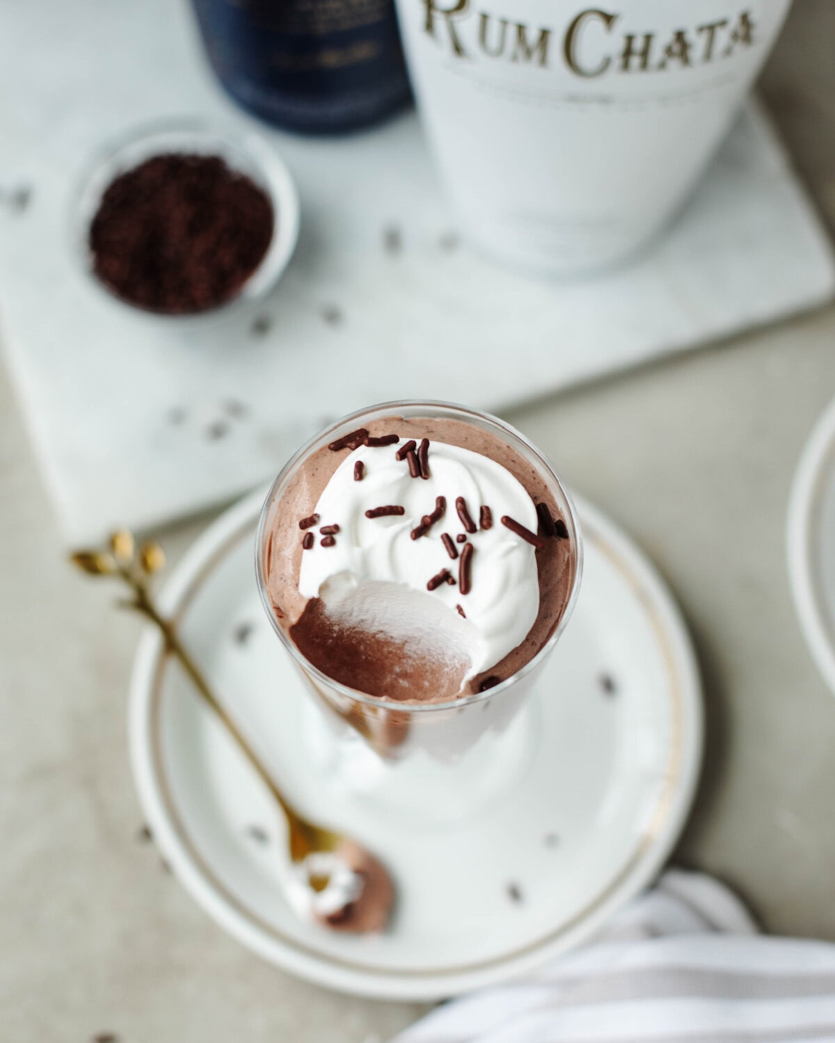 A glass filled with Rumchata pudding and whipped topping served with a spoon.