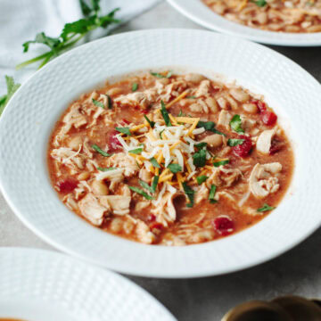 A white bowl filled with hearty chili topped with cilantro, shredded cheese.