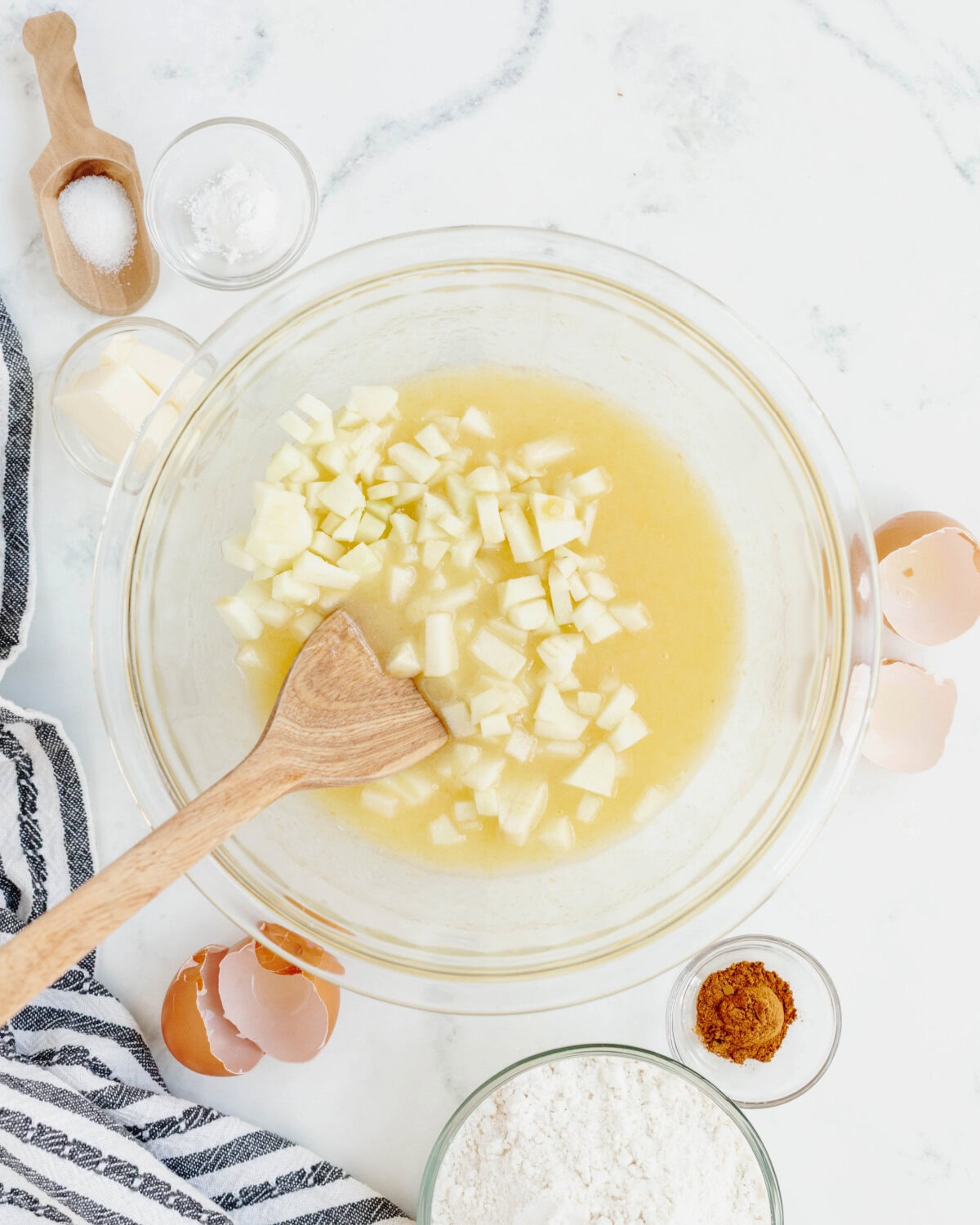 Eggs, buttermilk, and vanilla extract combined with diced apples in a glass mixing bowl.