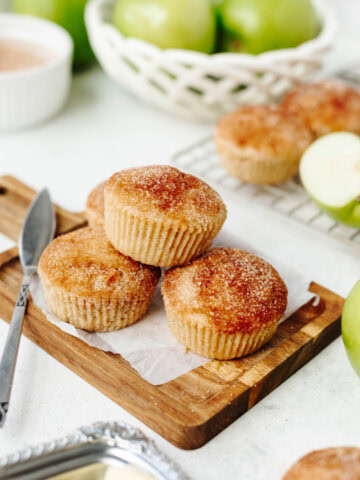 Stacked snickerdoodle apple muffins on a wood cutting board.