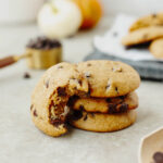 A stack of pumpkin chocolate chip cookies with a bite taken out to show the ooey gooey soft center.