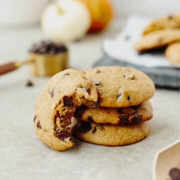 A stack of pumpkin chocolate chip cookies with a bite taken out to show the ooey gooey soft center.
