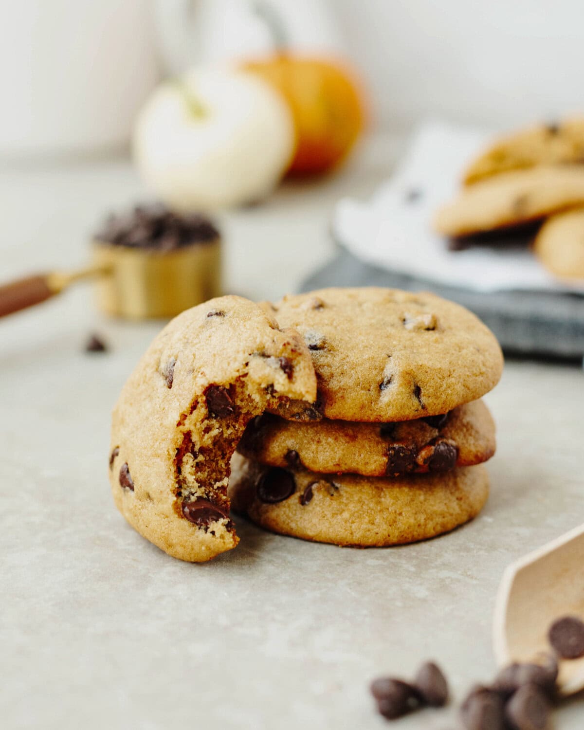 A stack of pumpkin chocolate chip cookies with a bite taken out to show the ooey gooey soft center.